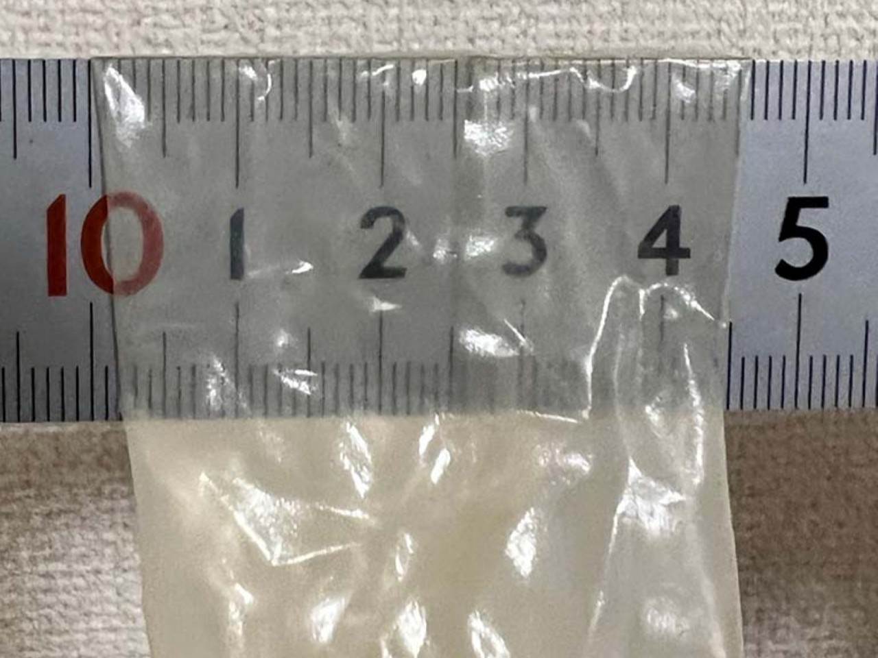 Kondom flach über ein Lineal gelegt, um die Breite in Millimetern sichtbar zu machen